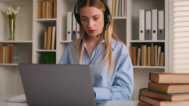 istock Caucasian woman in headset conference calling on laptop online teacher studying e-learning from home library with books writing notes write homework student girl learning computer distance education 2188401668