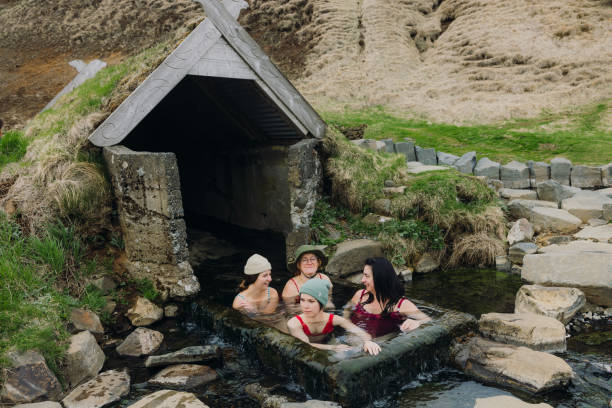 Group of cheerful multigenerational female travellers in red swimsuits having fun enjoying spa day floating in wild natural hot spring area in the mountains of Iceland