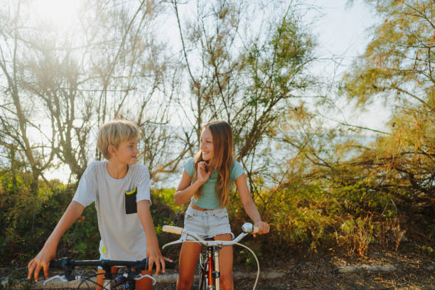 Photo of a smiling girl and boy riding bicycles together by the sea