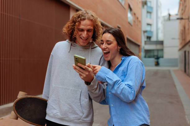 Young couple laughing while looking at smartphone in the city