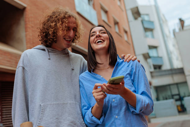 istock Young couple laughing while using a smartphone in the city 2188427511