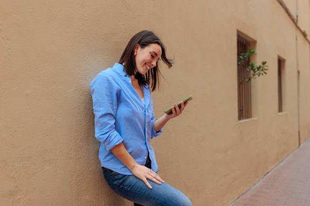 istock Young woman leaning against a wall and using a smartphone 2188427536