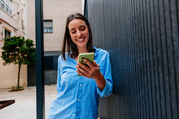 Young woman leaning against wall and using smartphone