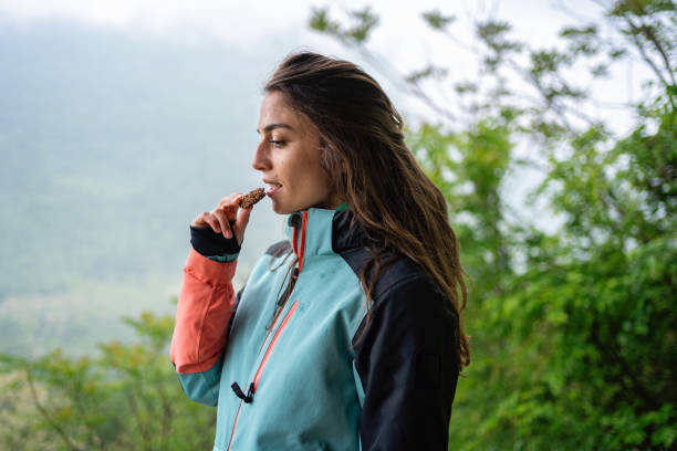 Young woman eats a healthy cookie as a snack while taking a break from hiking