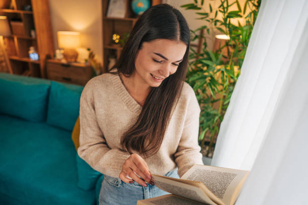 istock A woman standing by the window enjoying a peaceful moment while reading a book 2188432220