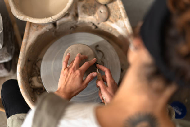 Young female ceramist shaping clay on pottery wheel in workshop