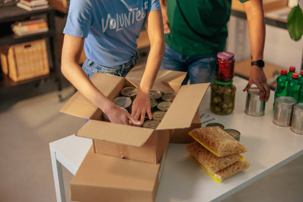 Donations packing for food bank Two volunteers arranging various food donations in cardboard boxes for distribution in a local charity food bank food bank stock pictures, royalty-free photos & images