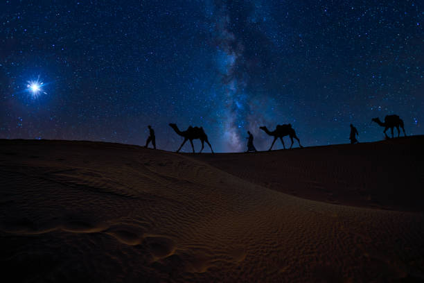 Christmas Jesus birth concept - Adoration of the Magi, Three Wise Men, Three Kings, and the Three biblical Magi with camel silhouettes journeying in sand dunes of desert follow Bethlehem star at night