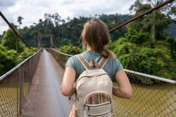 istock Young woman with backpack crossing a suspension bridge over a river 2188441753