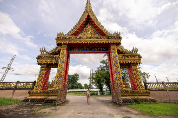 Woman strolling under elaborate archway adorned with intricate carvings. Tourist exploring cultural architecture. Beautiful day at a historical site.
