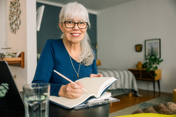 istock Smiling senior woman working from home taking notes in notebook 2188443780