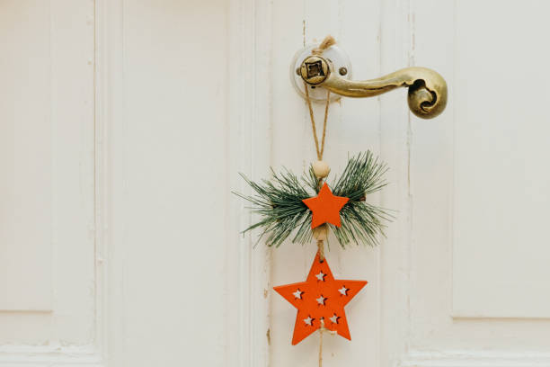 One holiday hanging decor of a red wooden star and a green Christmas tree branch with jute thread hanging on a retro white door handle in a home office during the day, side view close up. New Year concept, Merry Christmas, holiday decor.