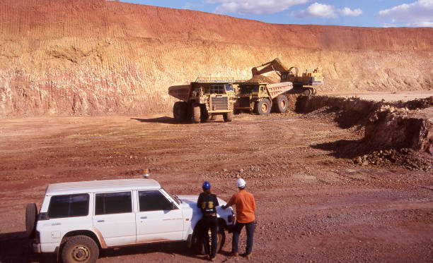 Tanami Desert, Northern Territory, Australia, January 7, 1987: Elevated view of open cut gold mine pit with two workers and vehicle in the foreground and heavy equipment and large dump truck in the Northern Territory, Australia