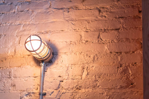 A warm industrial light fixture attached to a textured brick wall, casting a soft ambient glow. The scene evokes a cozy, rustic charm suitable for urban living spaces or modern interiors.