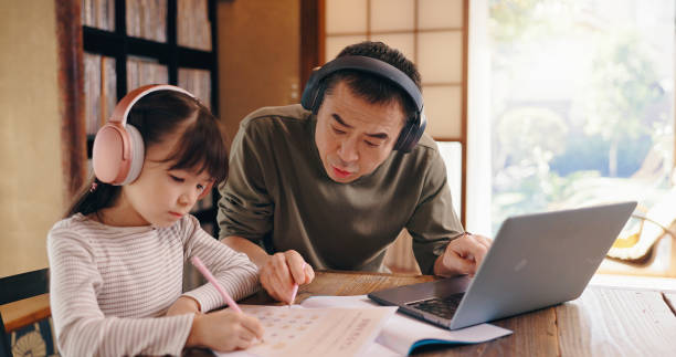 istock Asian dad, daughter and headphones with laptop for elearning, language tutoring or teaching at home. Japan, father or child writing with book or computer for online lesson or homeschooling at house 2188452553