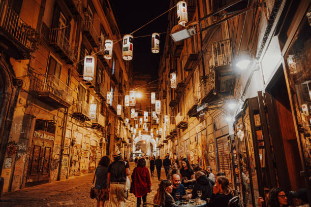 Naples, Italy, September 29, 2024: A bustling evening scene in Naples, Italy, showcasing people dining outdoors under decorative lanterns. The vibrant street is filled with warm lights and lively conversation.