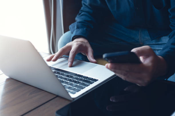 istock Man freelancer working on laptop and using mobile phone on wooden table at coffee shop, telecommuting 2188460474
