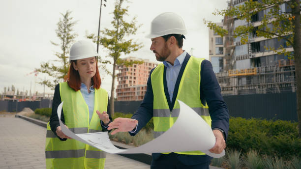 istock Two contractors civil engineers discuss electrical maintenance blueprint paper partnership discuss teamwork city buildings project construction builders woman man architects plan urban development 2188465139