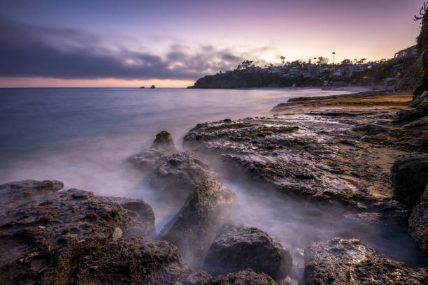 Waves gently lap against rocky shores as the sun sets over Crescent Bay Beach, creating a serene atmosphere in Laguna Beach, California.