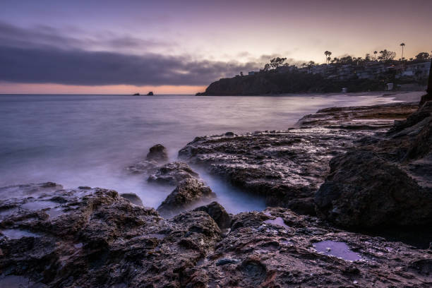 Waves gently crash on rocky shores as the sun sets over Crescent Bay Beach in Laguna Beach, California, creating a serene atmosphere.