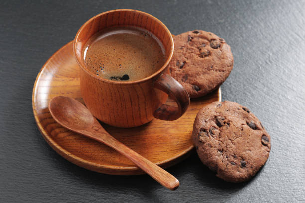 Cup of coffee and chocolate chip cookies on black stone background. Wooden dishes