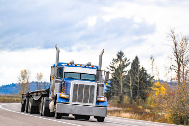 istock Blue classic American idol big rig semi truck tractor with empty flat bed semi trailer running on the turning autumn road 2188476463