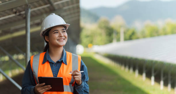 istock Female electrical engineer wearing hard hat using laptop checking solar panel farm equipment. Eco-friendly energy. Renewable clean energy technology concept. 2188479135