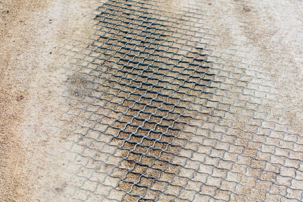 A dirty, worn out sidewalk with a black stain in the middle. The sidewalk is made of a mesh material and is located on a dirt road