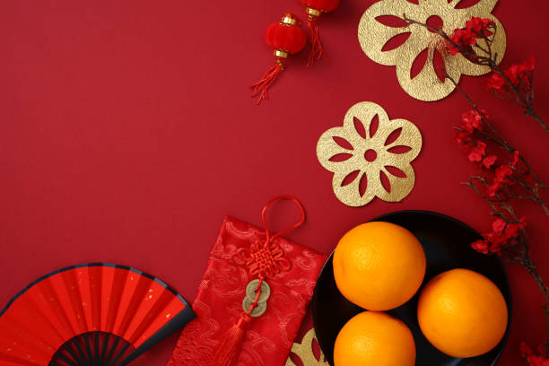 istock Chinese New Year concept featuring traditional decorations like red envelopes, oranges in a bowl, and golden paper cutouts on a rich red background. Flat lay, top view. 2188483452