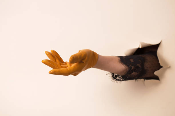 A woman's hand in a leather glove shows a gesture. The hand is pushed through a hole in beige paper.