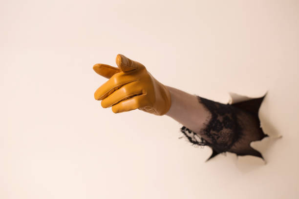 A woman's hand in a leather glove shows a gesture. The hand is pushed through a hole in beige paper.