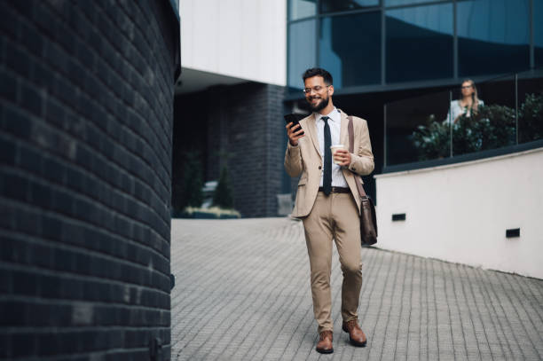 istock Smiling businessman walking and using smartphone app in city 2188483939