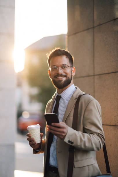 istock Smiling businessman using smartphone and holding coffee outside office building 2188483945