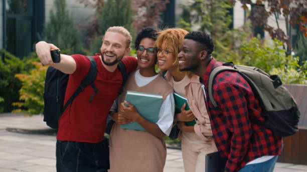 istock Happy smiling posing multiracial students diverse multiethnic friends university college campus outdoors after studying make selfie photo photography with mobile phone shooting video hugging high five 2188489557