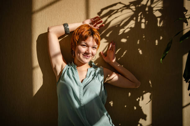 A charming woman, her red hair contrasting with a backdrop of artistic shadows, strikes a confident pose, creating a balance between light and darkness.