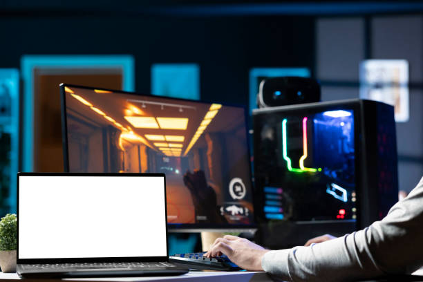 Man sitting on gaming chair using mockup laptop, relaxing by playing videogame on PC at computer desk late at night. Isolated screen notebook next to gamer enjoying game on computer