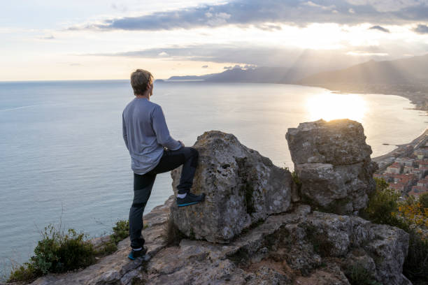 istock Young man pauses on promontory above sea at sunset 2188493956
