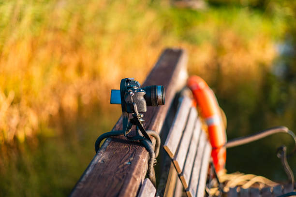 istock Digital Camera Resting on Wooden Bench Surrounded by Serene Nature Scene With Blurred Greenery and Vibrant Orange Life Buoy in Tranquil Setting 2188495180