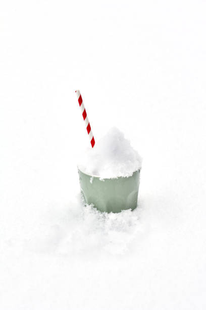 Green ceramic cup filled with snow and accented by a red and white striped straw, placed on a plain white snowy surface, showcasing a clean and minimal winter aesthetic