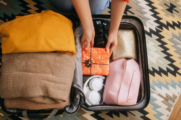 A woman carefully places a wrapped gift into a suitcase, preparing for a festive holiday trip