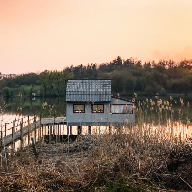 Small fishermen house on the end of the pier. Countryside scenery at sunset in the background.