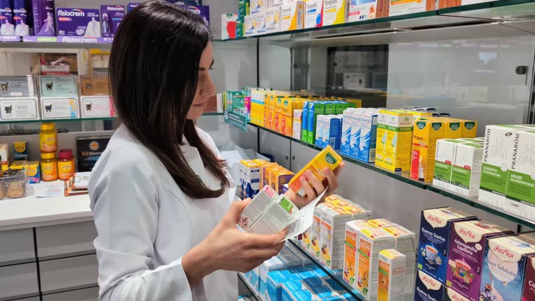 Young adult pharmacist organizes medicine boxes and packages on pharmacy shelves, maintaining efficient inventory management in a retail healthcare setting