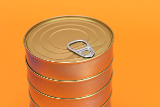 A Group of Stacked Tin Cans with Blank Edges on Orange Background. Canned Food. Different Aluminum Cans for Safe and Long Term Storage of Food. Steel Sealed Food Storage Containers