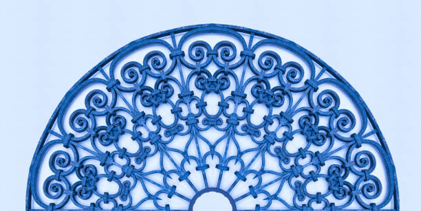 Fort de France, Martinique, West Indies. \nA detailed close-up of a red rooster weather vane mounted on the top of a geometric blue metal gate, featuring diamond patterns and a circular cutout. The gate is set against a plain white wall with subtle shadows indicating daylight. The structure appears vintage and decorative, possibly part of a residential or urban facade in a Mediterranean-style location. No people are present. The image conveys a sense of traditional craftsmanship and architectural detail, suitable for commercial uses such as travel articles on European villages, home decor inspiration, cultural heritage illustrations, or background elements in lifestyle magazines focusing on wrought iron designs.
