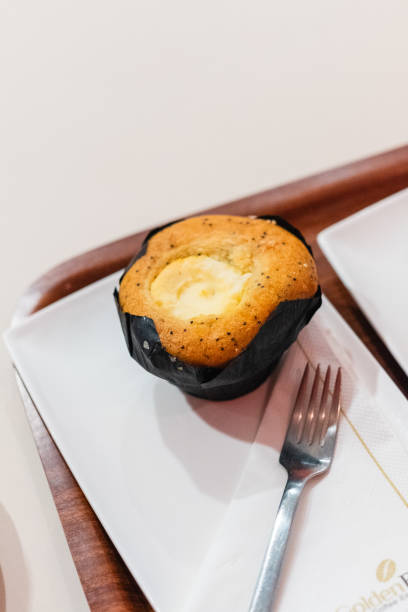 Close-Up of Delicious Vanilla Muffin With Cream Filling on a White Plate, Accompanied by a Fork. Perfect for Breakfast or Dessert. Captures the Essence of Bakery Freshness and Culinary Delight.