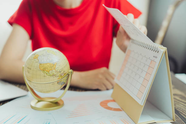 istock person in red shirt examines calendar and globe, analyzing data charts on table. This scene reflects planning and organization in professional setting 2188513982