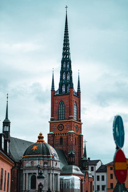 istock Historic Brick Church Architecture with Gothic Spires Under Cloudy Sky in Urban Setting, Showcasing Timeless European Design and Religious Heritage Amidst Modern Cityscape Elements 2188514050