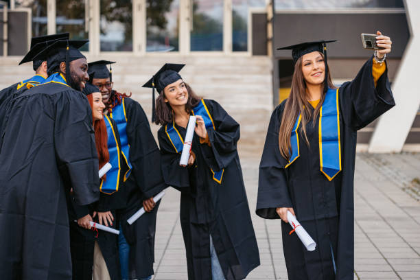 istock Students In Graduation Gowns Taking Selfies Using Phone On The University Campus 2188517583
