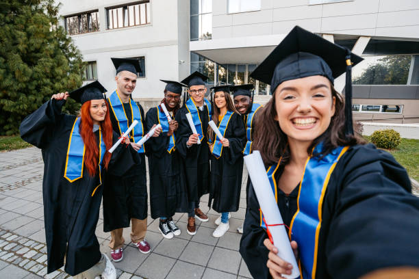 istock Students In Graduation Gowns Taking Selfies On The University Campus 2188517623