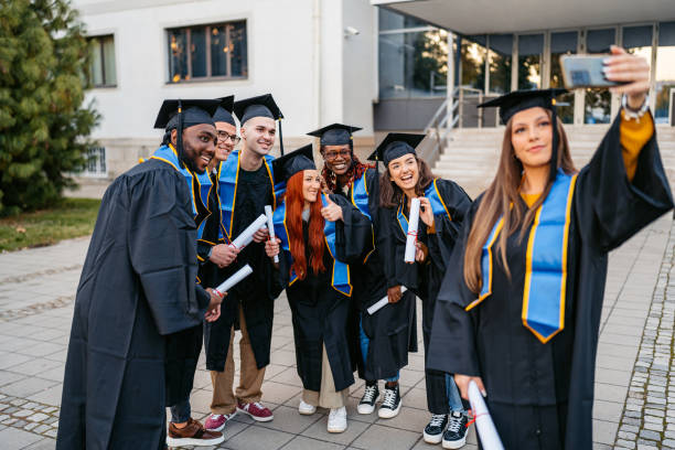 istock Students In Graduation Gowns Taking Selfies Using Phone On The University Campus 2188517638